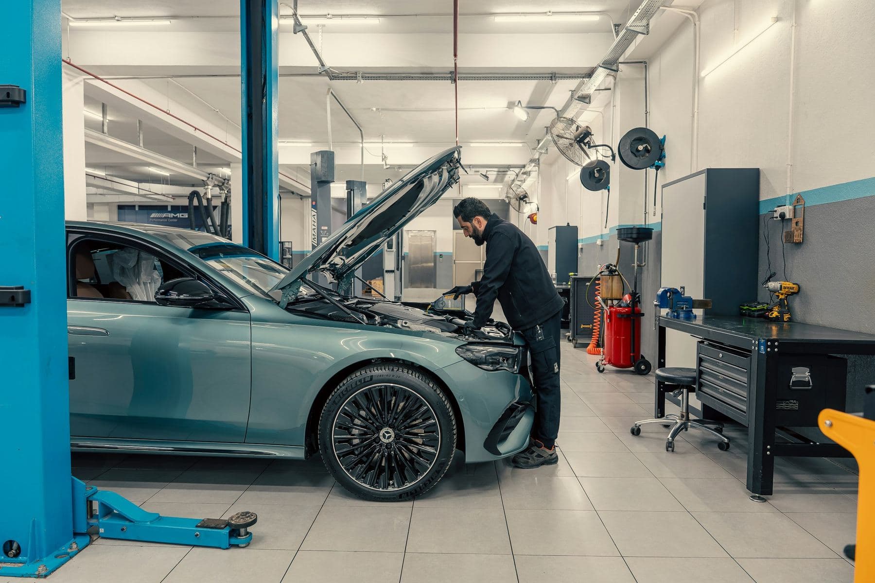 Technician working under the open hood of a car in a bright service bay